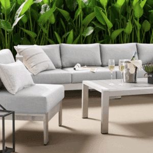 Modern outdoor sectional patio set with gray cushions and aluminum frame, arranged with a sofa, chairs, and a coffee table against lush greenery.